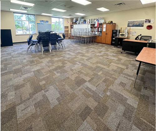 carpet on a floor with chairs stacked in the middle and desks in the back corner